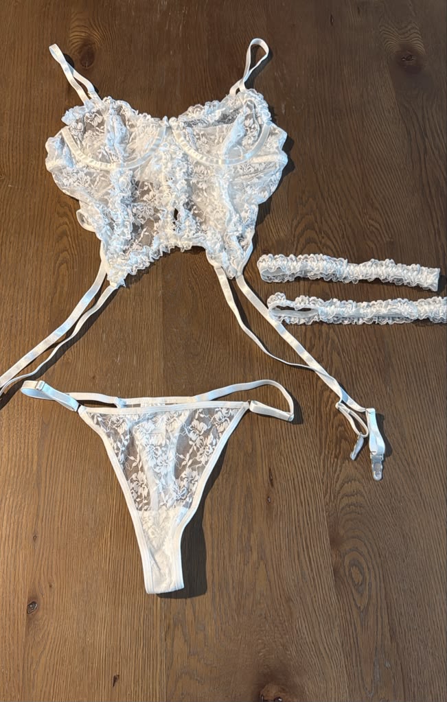 White bridal lace 3-piece lingerie set with bustier, thong and matching garter straps laid flat.
